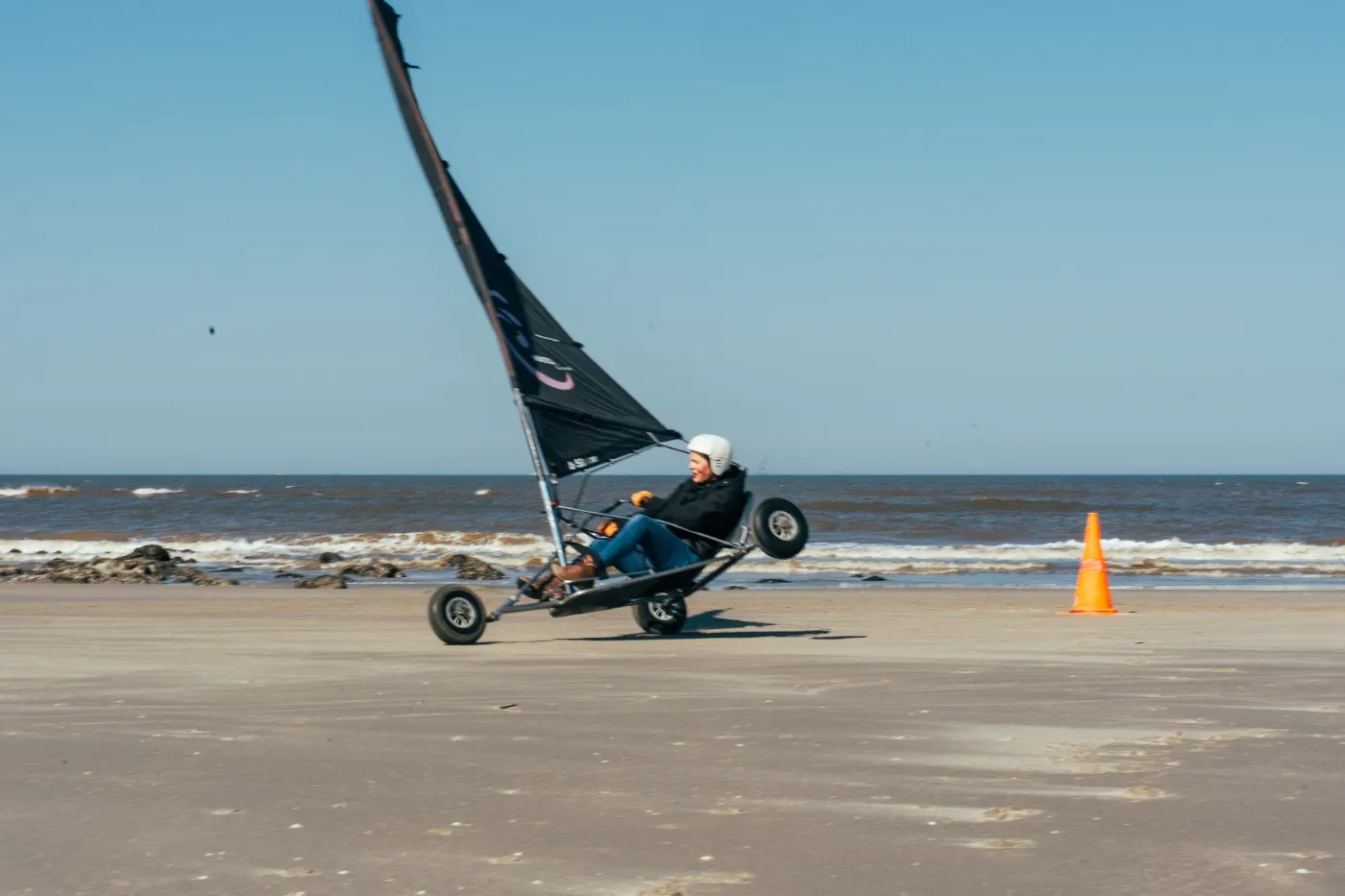 Deelnemer hangt uit de blokart in volle vaart op het strand